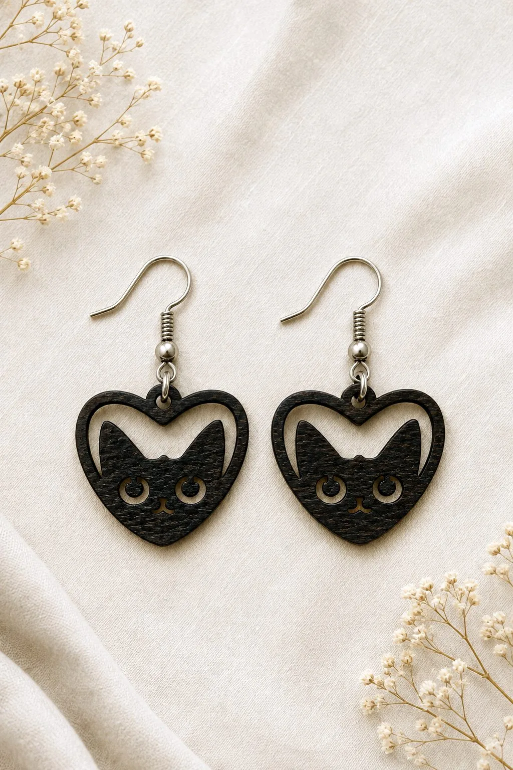 Close-up of dark wooden heart earrings with a cat face cut into them, cat laser cut earring SVG from svgdiy.com