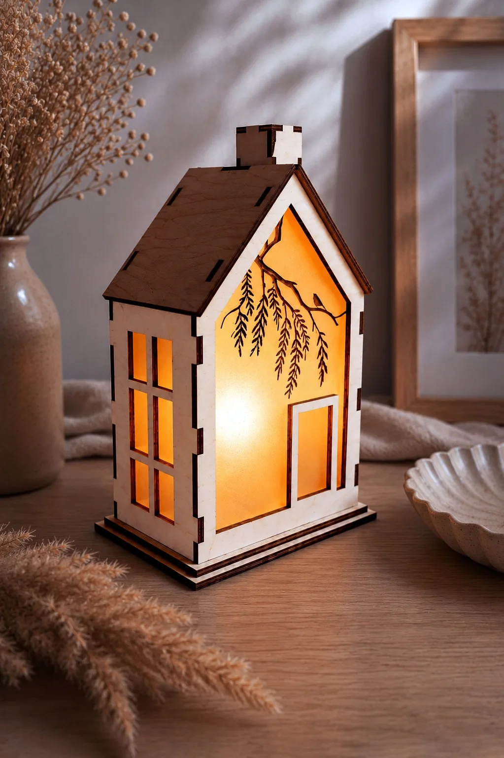 A wooden lantern house with a willow branch and a small bird engraved on the lit gable panel and a paned side window, free laser cut night light SVG from svgdiy.com