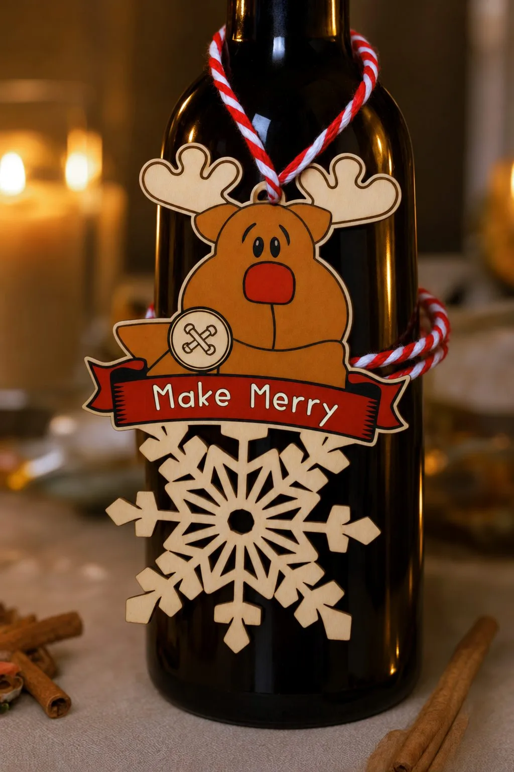 The Make Merry reindeer snowflake ornament tied with red and white twine around the neck of a dark bottle, next to candles and cinnamon sticks, free download link at svgdiy.com